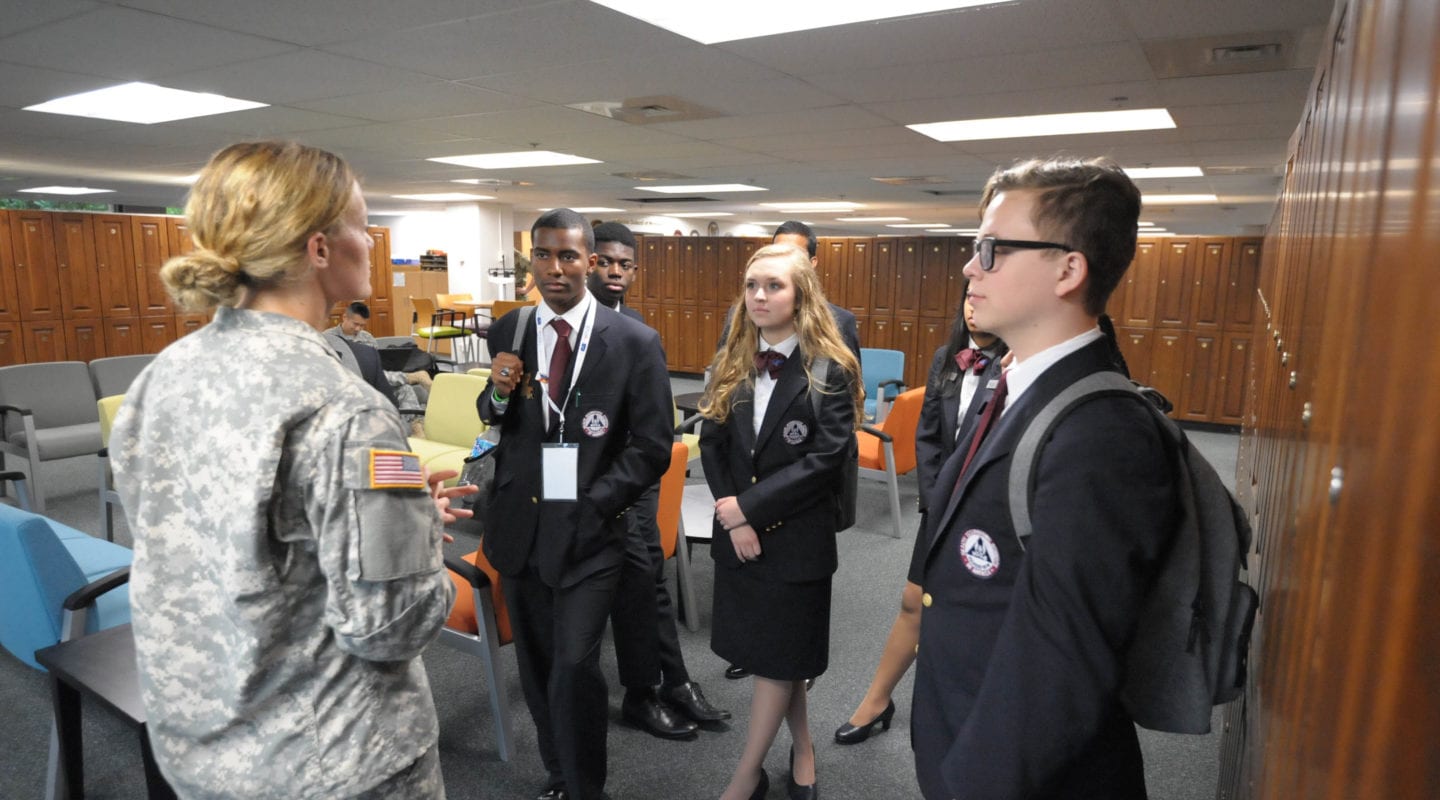 Woman in military uniform talking to HOSA students in professional blue blazers