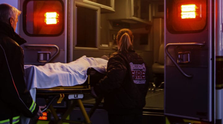 Male paramedic and female EMT in fire department coats loading a patient on a cot into the back of an ambulance