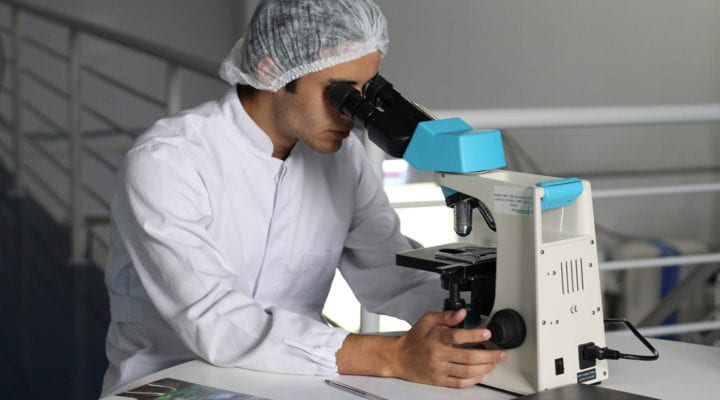 Man in a lab coat looking through a microscope in a lab
