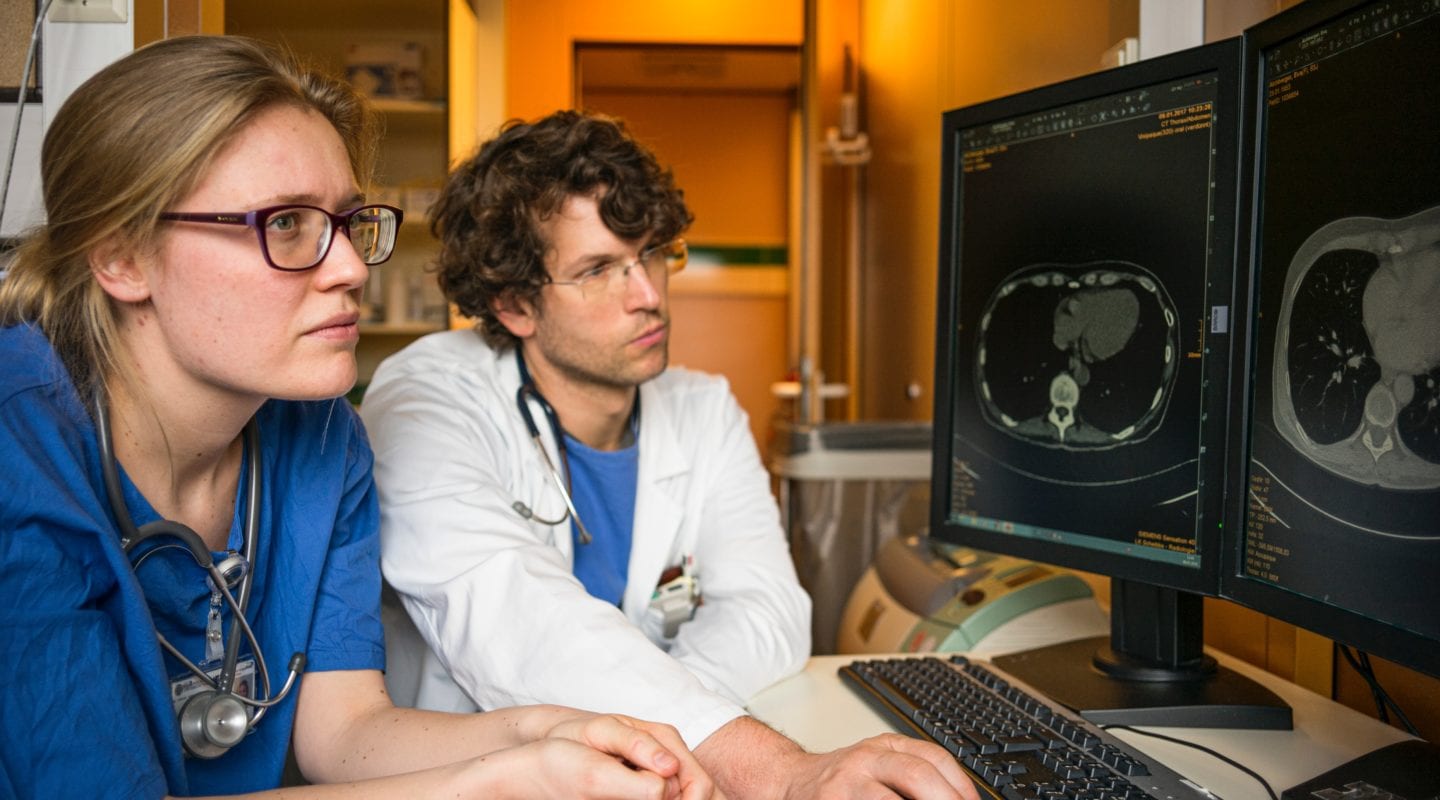 Woman with glasses in scrubs and man in glasses with scrubs and lab coat looking at a transverse abdominal MRI