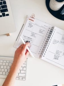 Hand putting a sticky note in a planner with a computer in view