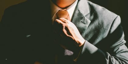 Photo of man wearing a blazer and tie straightening his tie