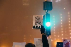 Hand holding up a sign that reads, "Do not wait for leaders, become them"